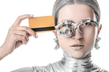 silver robot touching head with credit card and looking at camera isolated on white, future technology concept clipart