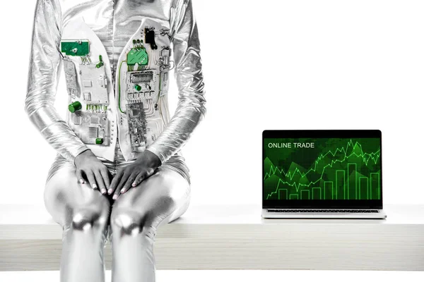 kırpılmış görüntü izole beyaz, geleceğin teknoloji kavramı üzerinde online ticaret cihazı ile dizüstü yakınındaki masada oturan bir robot