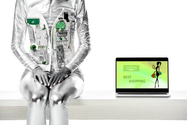 cropped image of robot sitting on table near laptop with best shopping appliance isolated on white, future technology concept