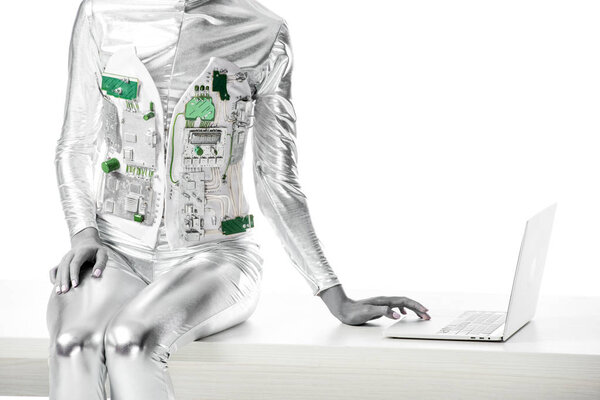 cropped image of robot sitting on table and using laptop isolated on white, future technology concept