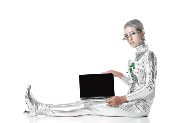 Silver robot sitting and showing laptop with blank screen isolated on white, future technology concept
