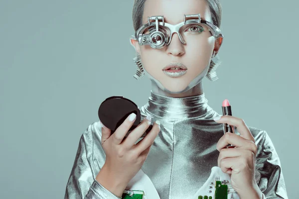 silver robot holding mirror and lipstick isolated on grey, future technology concept
