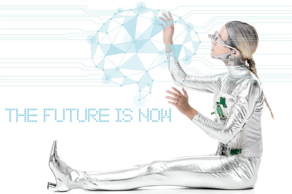 боковой вид серебряного киборга, сидящего и трогающего цифровые данные, изолированные на белом фоне с подписью "будущее сейчас"
