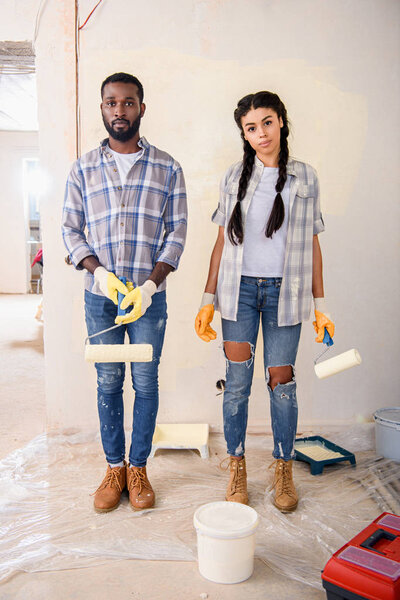 young couple with rolling brushes looking at camera during renovation of home