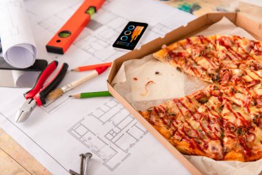 close-up shot of box with pizza, tools and smartphone with charts on screen on building plan clipart