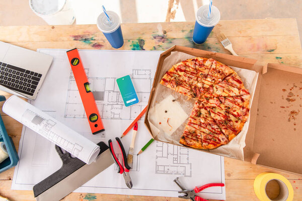 top view of box with pizza, tools and smartphone with twitter app on screen on building plan