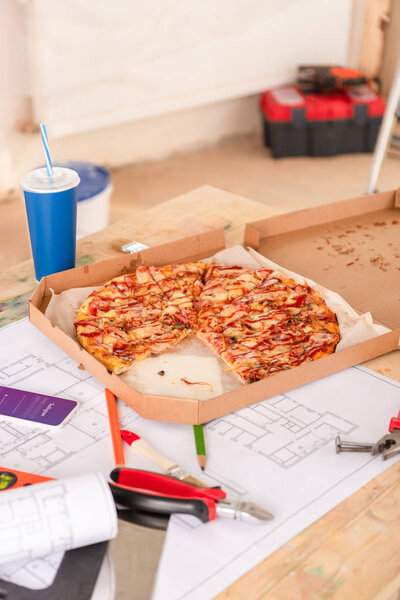 selective focus of pizza, soda, blueprint, tools and smartphone with instagram on screen on table