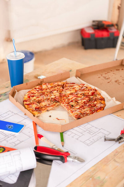 selective focus of pizza, soda, blueprint, tools and smartphone with shazam on screen on table