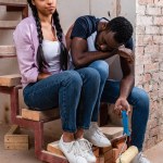 Joven afircan americana mujer animando cansado novio con pintura rodillo durante la renovación de casa