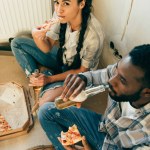 Vista ad alto angolo di coppia afro-americana mangiare pizza e bere birra durante la ristrutturazione a casa