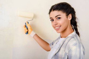 selective focus of happy african american woman painting wall  clipart