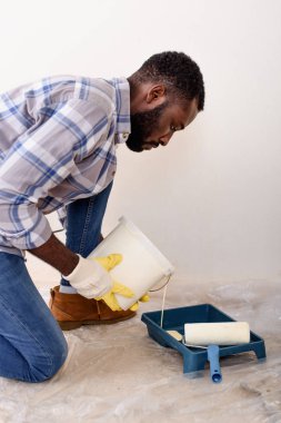 Koruyucu eldiven ev yenileme sırasında boya silindiri tepsi içine dökme Afro-Amerikan erkek odaklı