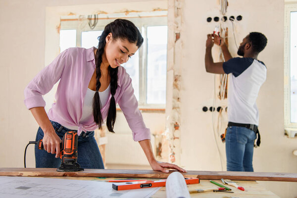 привлекательная африканская американка, работающая с мозаикой, пока ее бойфренд стоит позади во время ремонта дома

