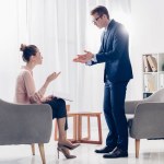 Irritated businessman standing and gesturing while giving interview to journalist in office