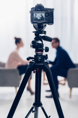 side view of businessman giving interview to journalist in office, camera on tripod on foreground clipart