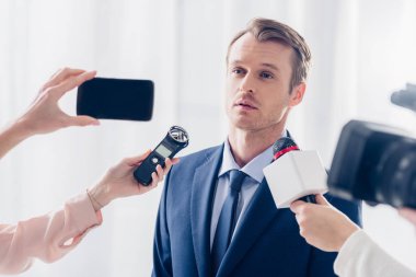 handsome businessman giving interview to journalists and looking away in office clipart