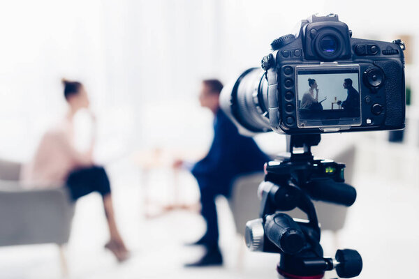 businessman giving interview to journalist in office, camera on tripod on foreground