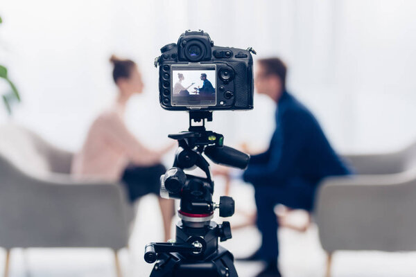 бизнесмен дает интервью журналисту в офисе, камера на штативе на переднем плане
