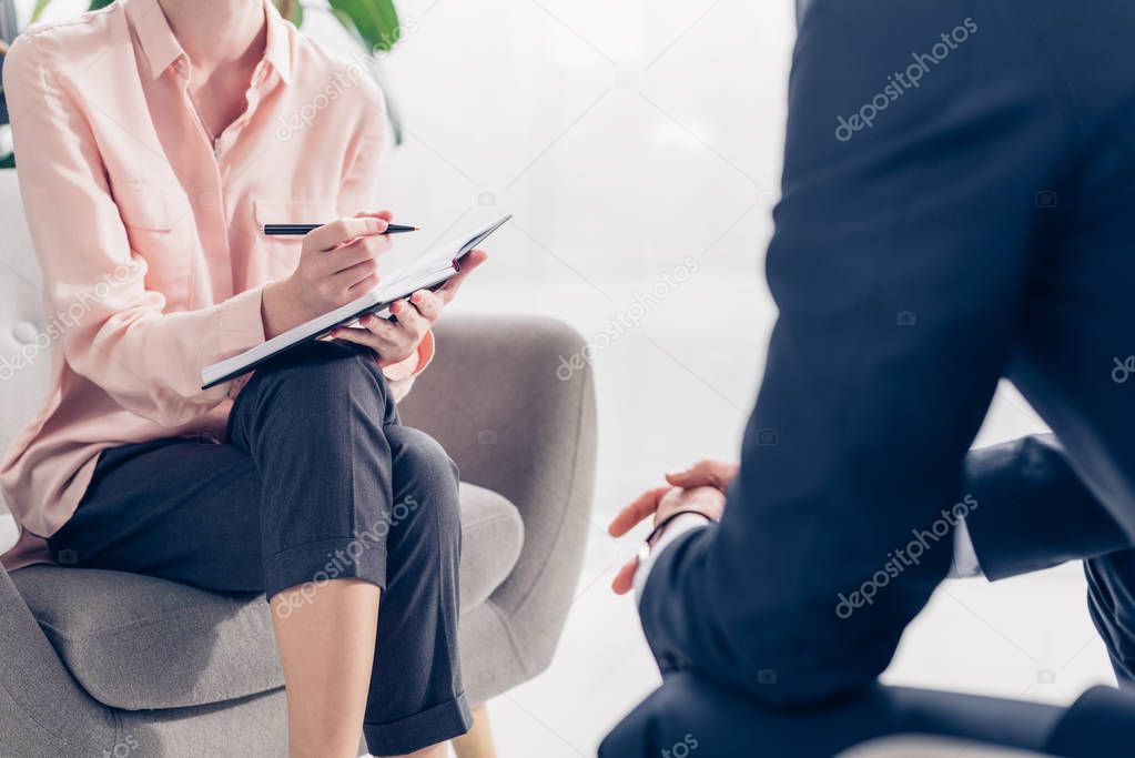 cropped image of journalist taking notes during interview with businessman in office
