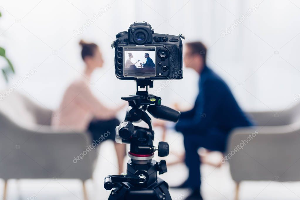 businessman giving interview to journalist in office, camera on tripod on foreground