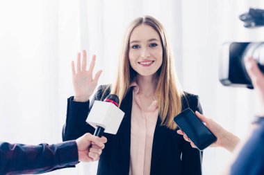 Gazeteciler için röportaj veren ve ofiste el sallayarak gülümseyen çekici iş kadını