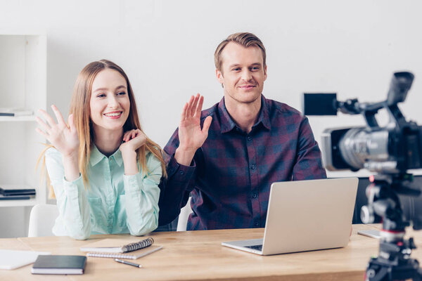 smiling video bloggers recording vlog and waving hands in office