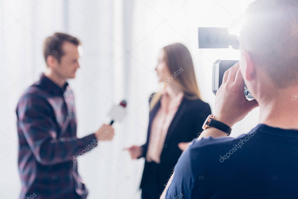 selective focus of businesswoman in suit giving interview to journalist at workspace