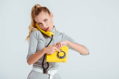 beautiful woman dialing phone number on vintage yellow telephone isolated on grey clipart