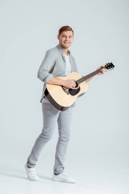 kameraya bakarak ve gri arka plan üzerinde akustik gitar çalmak gri giyim gülümseyen adam