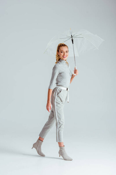 woman in grey clothes looking at camera and posing with transparent umbrella on grey background