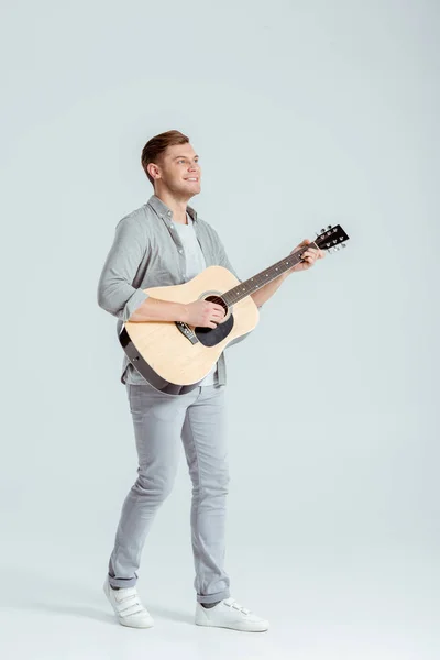 灰色の背景でアコースティック ギターを弾くグレーの服でハンサムな男 — ストック写真