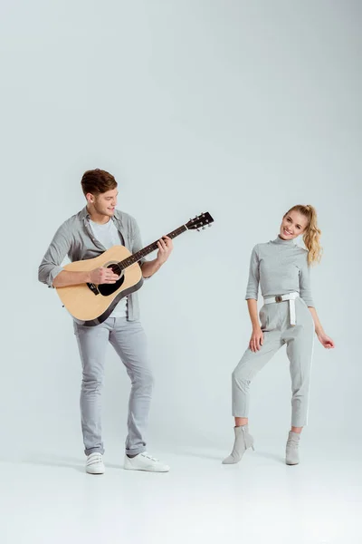 Mann Spielt Akustikgitarre Während Lächelnde Frau Auf Grauem Hintergrund Tanzt — Stockfoto