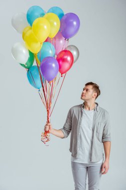 yakışıklı adam gri arka plan üzerinde renkli balon demeti holding