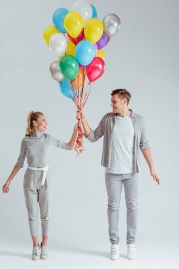 mutlu çift ayakta sessizce ve gri arka plan üzerinde renkli balon demeti holding