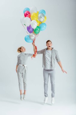 heyecanlı çift gri arka plan üzerinde renkli balon demeti ile atlama