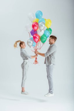 gri giyim gri arka plan üzerinde renkli balon demeti ile atlama içinde çift