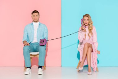 konuşmayı sıkılmış adam mor vintage telefon pembe ve mavi arka plan üzerinde tutan kadın