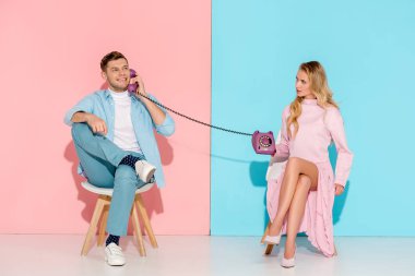 Mor vintage telefon gülümseyen adam pembe ve mavi arka plan ile konuşurken tutan memnun kadın