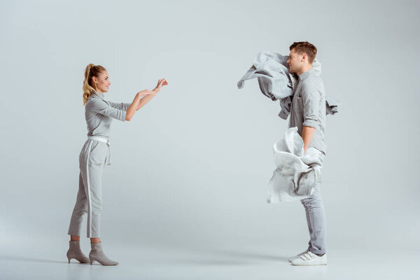 attractive woman throwing pile of clothes at man on grey background