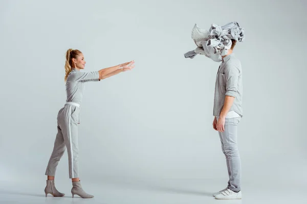 blonde woman throwing pile of clothes at man on grey background