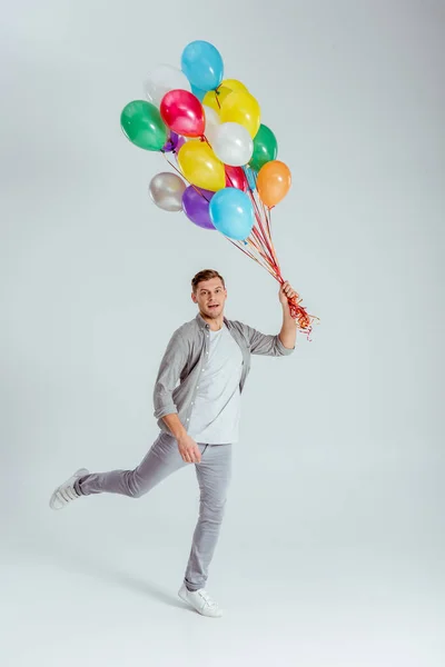 Man Jumping Bundle Colorful Balloons Looking Camera Grey Background — Stock Photo, Image
