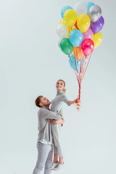 Pareja Abrazándose Mientras Sonríe Mujer Sosteniendo Paquete Globos Colores Aislados — Foto de Stock