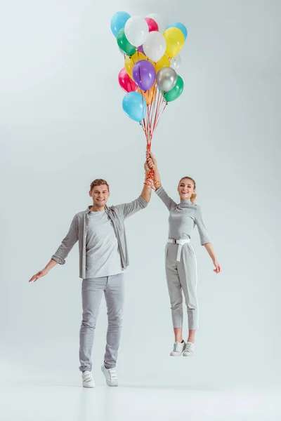 灰色の背景に色とりどりの風船の束をジャンプ美しい幸せなカップル — ストック写真