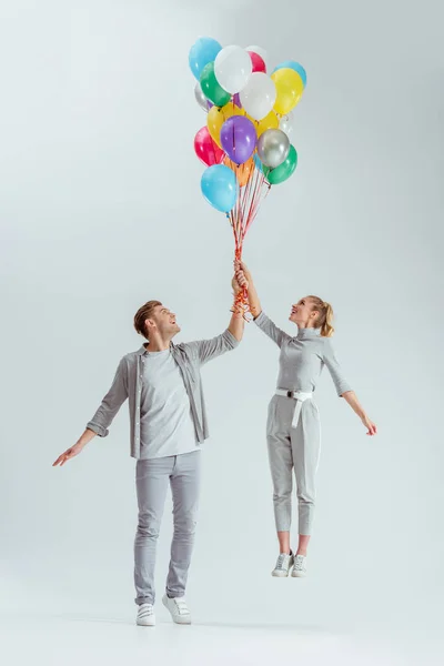 Happy Couple Jumping Bundle Colorful Balloons Grey Background — Stock Photo, Image