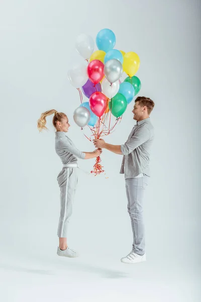 Cuplu Îmbrăcăminte Gri Sărind Pachet Baloane Colorate Fundal Gri — Fotografie, imagine de stoc