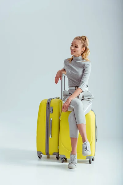 旅行の概念 灰色の背景に胡坐でスーツケースの上に座って美しい女性 — ストック写真