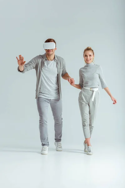 男の灰色の背景に仮想現実を体験しながら手を繋いでいるカップルを笑顔  — 無料ストックフォト
