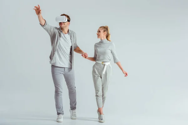 男の仮想現実を体験し 灰色の背景でジェスチャーしながら手を繋いでいるカップル — ストック写真