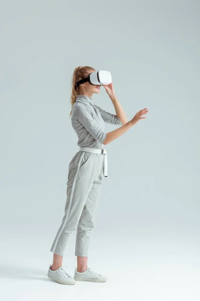 仮想現実の灰色の背景上の経験をしながらジェスチャー グレーの服と ヘッドセットの女の子 — ストック写真