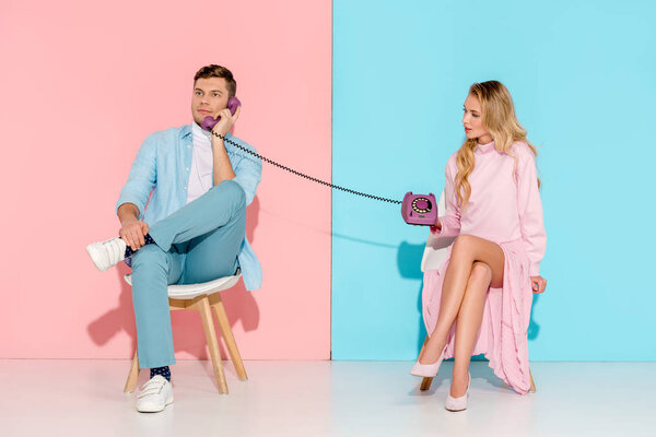 dissatisfied woman holding purple vintage telephone while man talking with pink and blue background